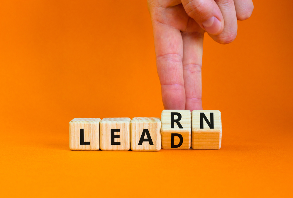 Learn and lead symbol. Businessman turns wooden cubes, changes the word 'learn' to 'lead'. Beautiful orange table, orange background. Business, educational, learn and lead concept. Copy space.