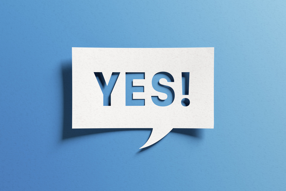 Yes sign showing positive answer, joy, agreement, celebration, affirmative decision or determination. Word yes on cutout paper speech buble on blue background.
