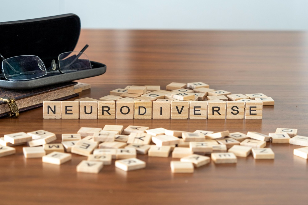 neurodiverse word or concept represented by wooden letter tiles on a wooden table with glasses and a book