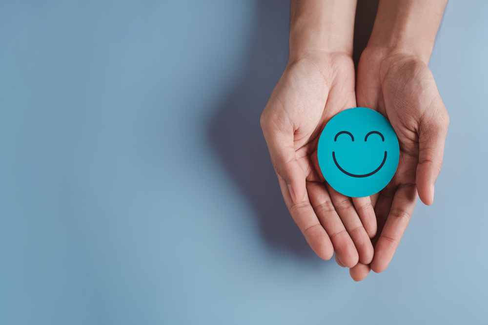 Hands holding blue happy smile face, good feedback rating, positive customer review, experience, satisfaction survey, smiley mental health, child wellness, world mental health day on blue background