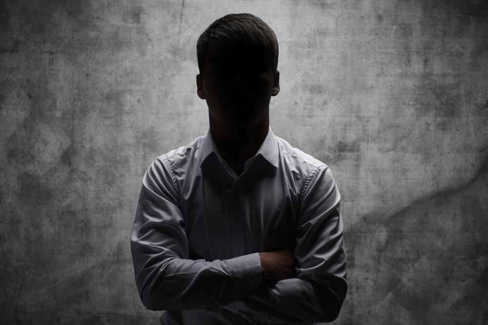 Anonymous man in a business shirt with arms crossed against a dark background
