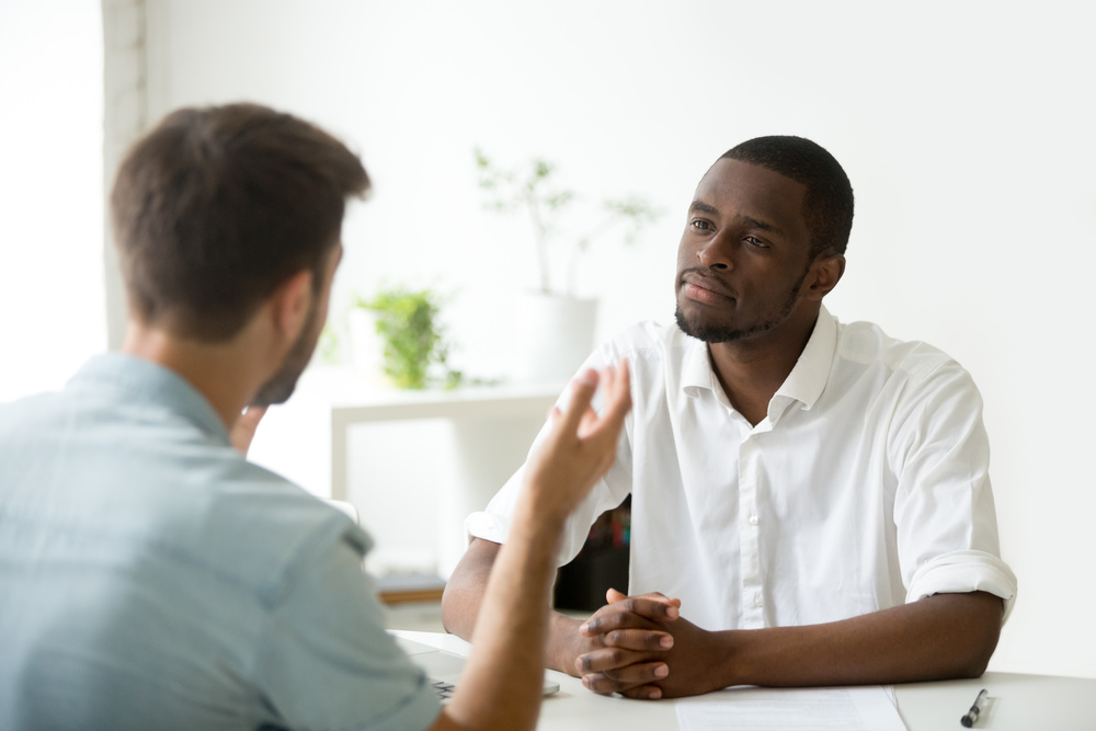 African American employer listening attentively to caucasian job applicant talking at work interview, being friendly and interested to candidate. Concept of recruiting, employment, hiring