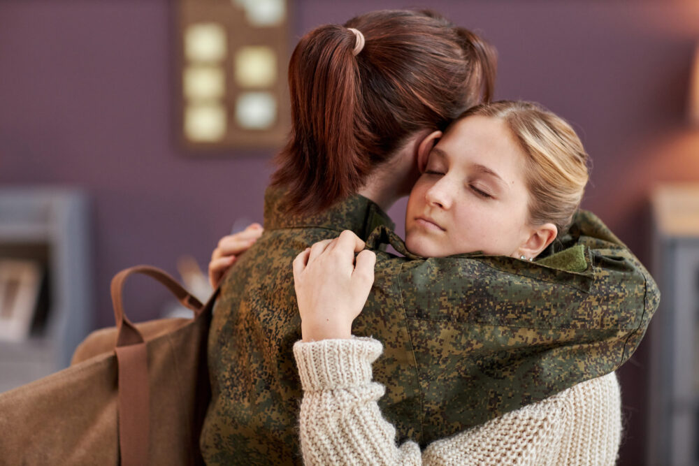 Side view portrait of teen girl embracing mother working in military with eyes closed, copy space