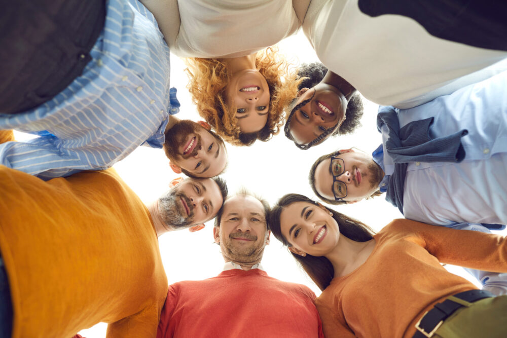 Low angle portrait of diverse team of happy people huddling in corporate meeting