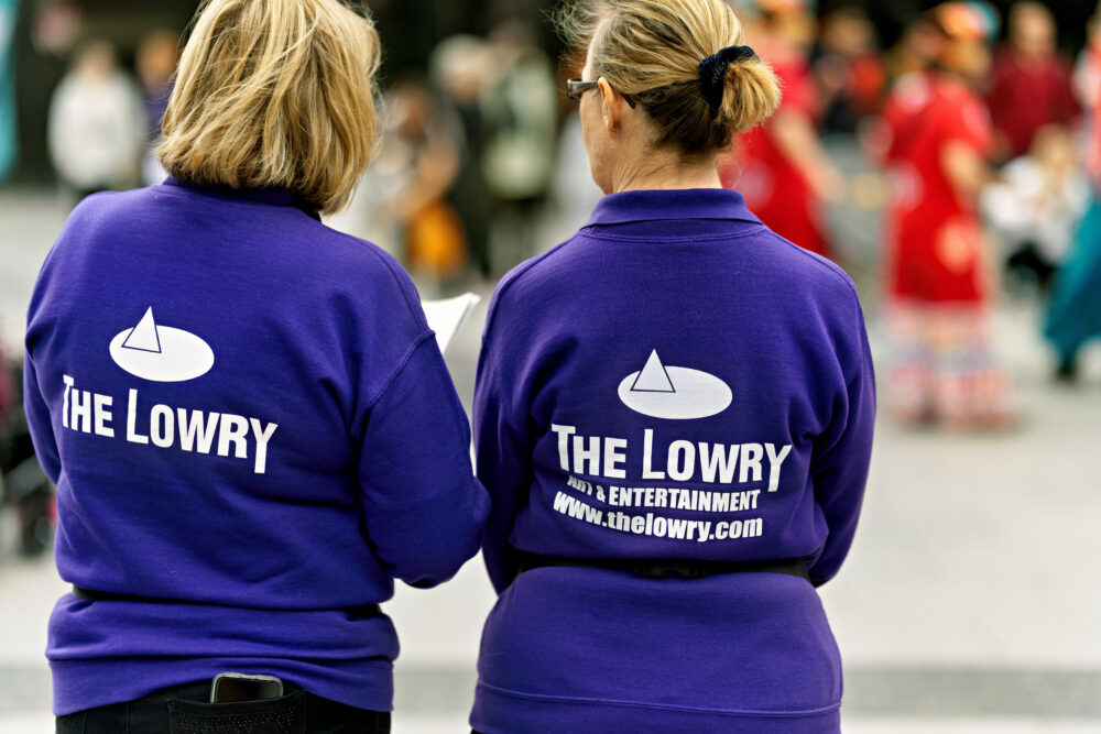 Salford UK 06 Aug 2023 two ladies employee's standing with there backs to the camera with the Lowry theatre logo on the backs of there purple jackets