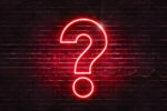 Neon sign on a brick wall in the shape of a question mark.(illus