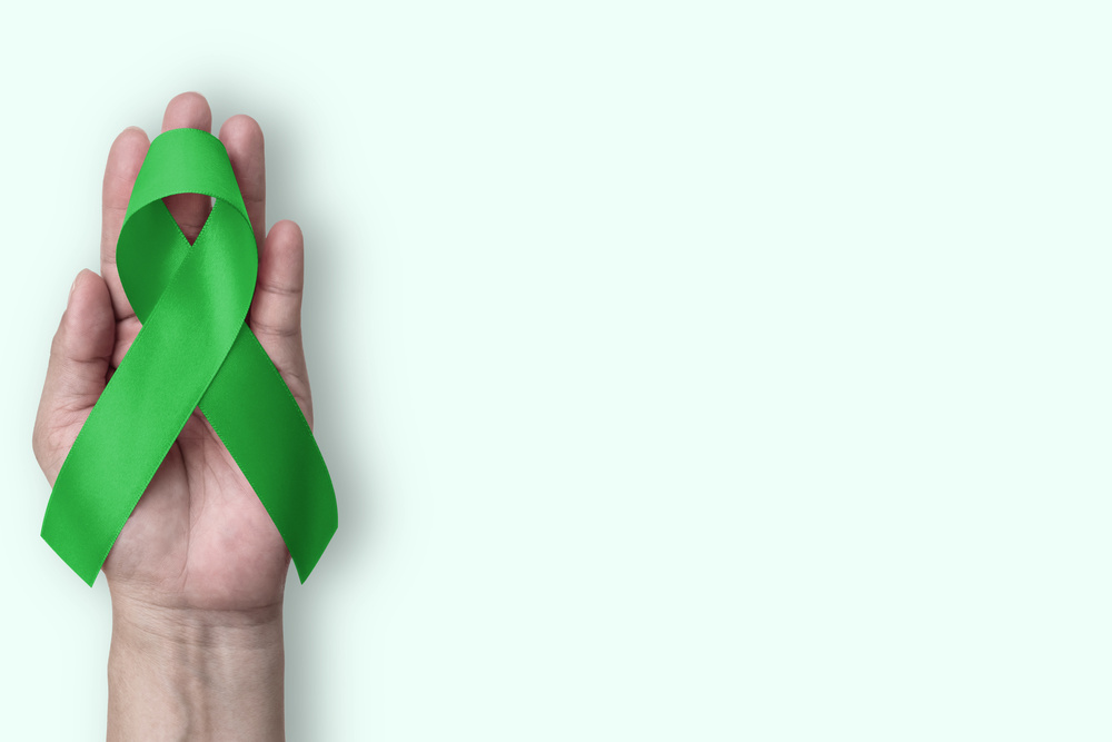 Green ribbon for gallbladder and bile duct cancer awareness month in February, bipolar disorder, mental health illness with kelly green bow isolated on hand support background