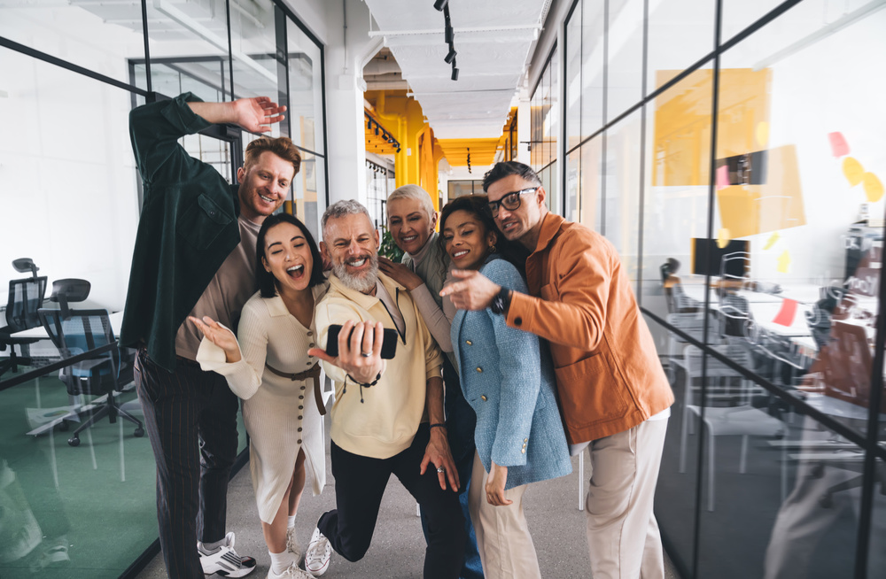 Group of cheerful multiethnic friends taking selfie together while standing near office entrance