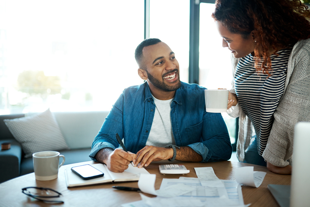 Couple talk about budget, finance and bills with paperwork of financial information, happy with savings and income. Mortgage, insurance and taxes, man and woman laugh together with home bookkeeping.