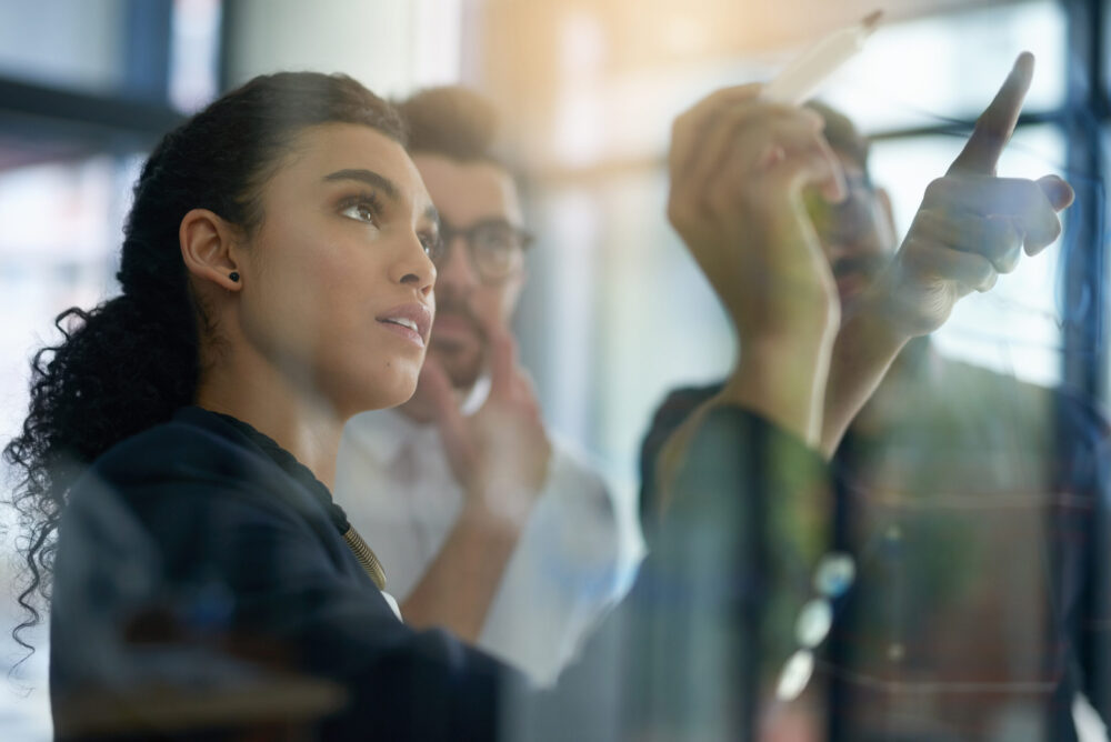 Succeeding is top priority. Shot of a group of colleagues brainstorming together on a glass wall in an office.