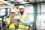 A portrait of an industrial man and woman engineer with tablet in a factory, talking.