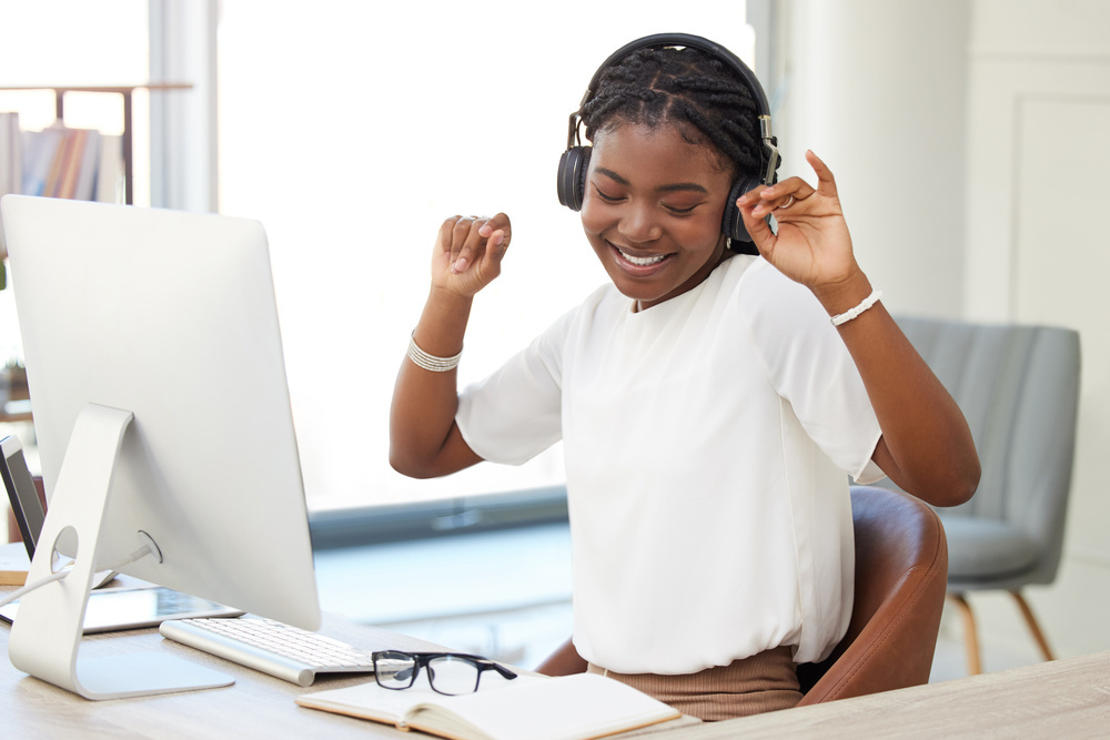 Dance, headphones and woman on computer, office or workplace for mental health, wellness and listening. Happy african person working on desktop pc and dancing to music, celebration and job or career