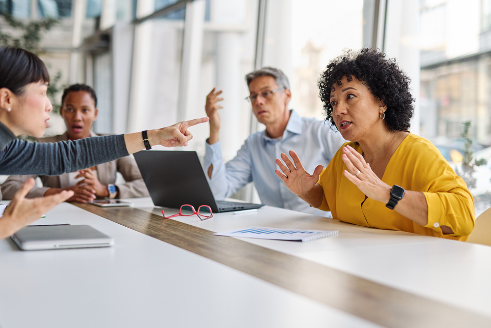 A group of businesspeople are gathered around a table, discussing something. Scene is serious and focused, as the group appears to be engaged in a discussion or decision-making process. There is a lot of frustration and argument