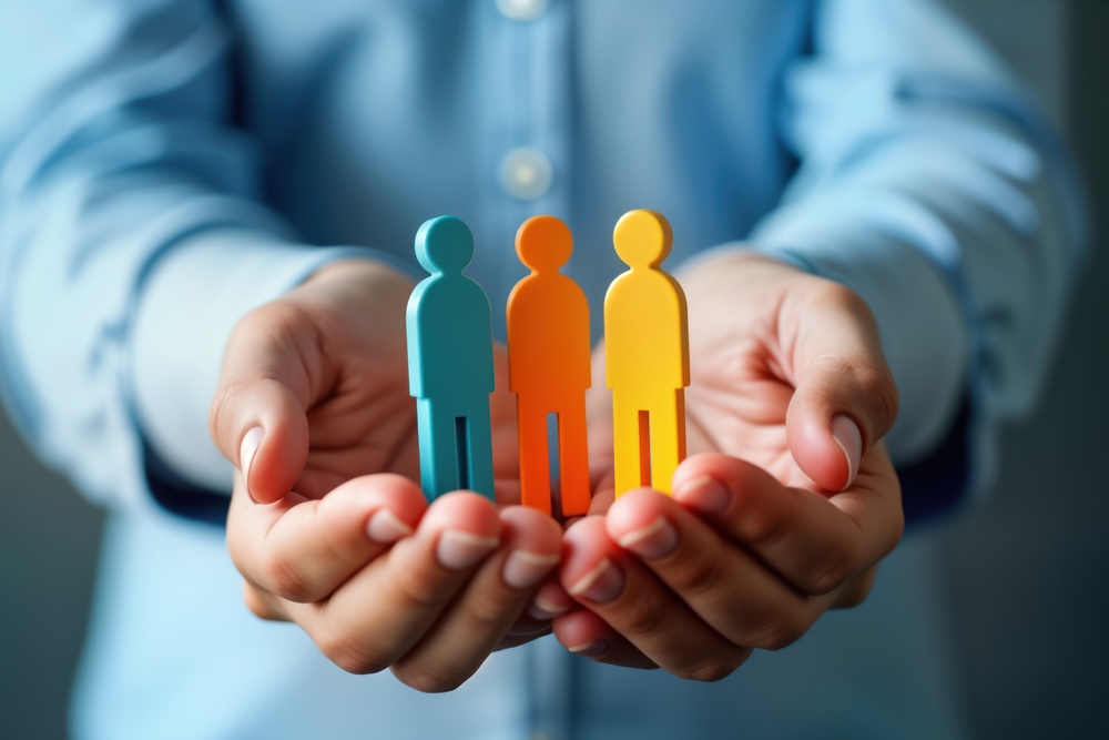 Hands hold three colorful figurines representing employees. Care, support of employees key. Human resource management enhances well-being, performance. Workplace culture of care recognition for