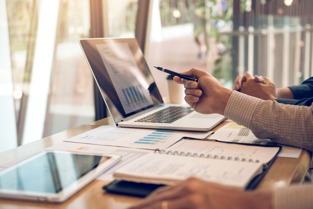 Business partnership pointing to the graph of the company financial statements report and profits earned during in the computer screen with giving a presentation to colleagues in office room.