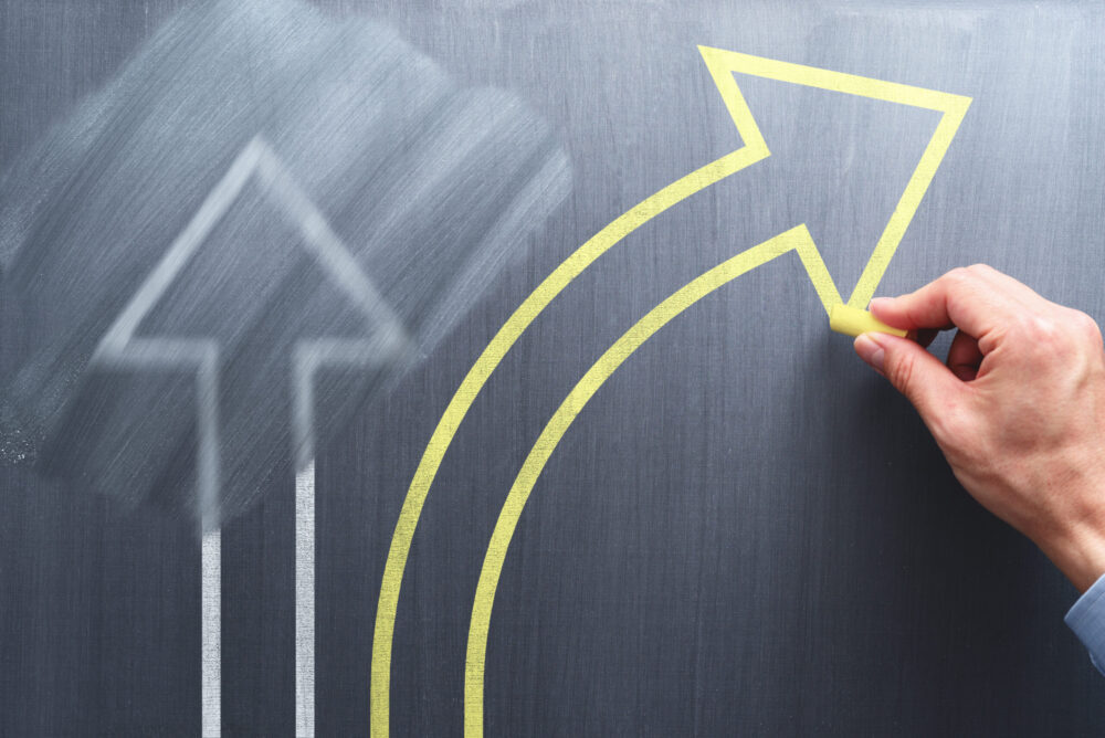 Changing business management concept. Businessman erasing white arrow and drawing yellow arrow on chalkboard.