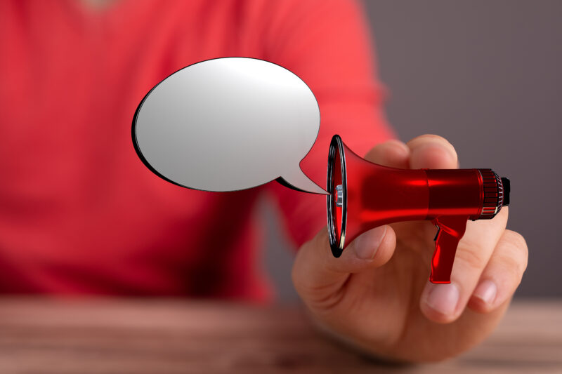 Person holding a megaphone with a speech bubble, symbolising cutting through noise in workplace health and wellbeing communications