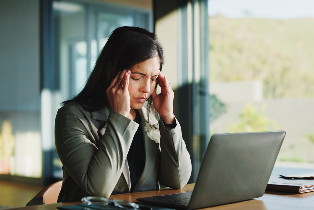 Frustrated, business woman and headache with laptop, stress or overworked for pressure in office. Tired, female person or employee with migraine, fatigue or burnout for mental health in workplace