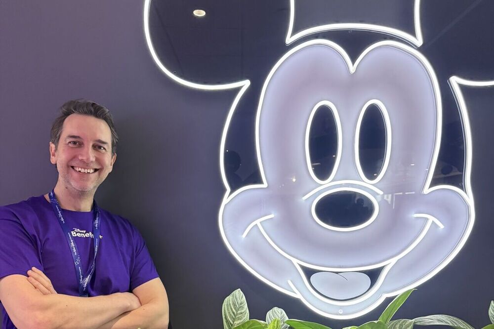 Striking LinkedIn photo of Max Landry, co-founder, Euphoric, in front of a back-lit image of Mickey Mouse, adding a playful touch to his new client-win announcement on LinkedIn