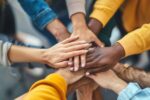 Diverse team hands joined in a circle symbolising inclusion, belonging and wellbeing at work