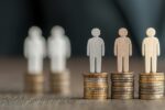 Cardboard cut-out figures standing on equal-height stacks of coins, symbolising financial inclusion and fair access to workplace savings and financial wellbeing opportunities.