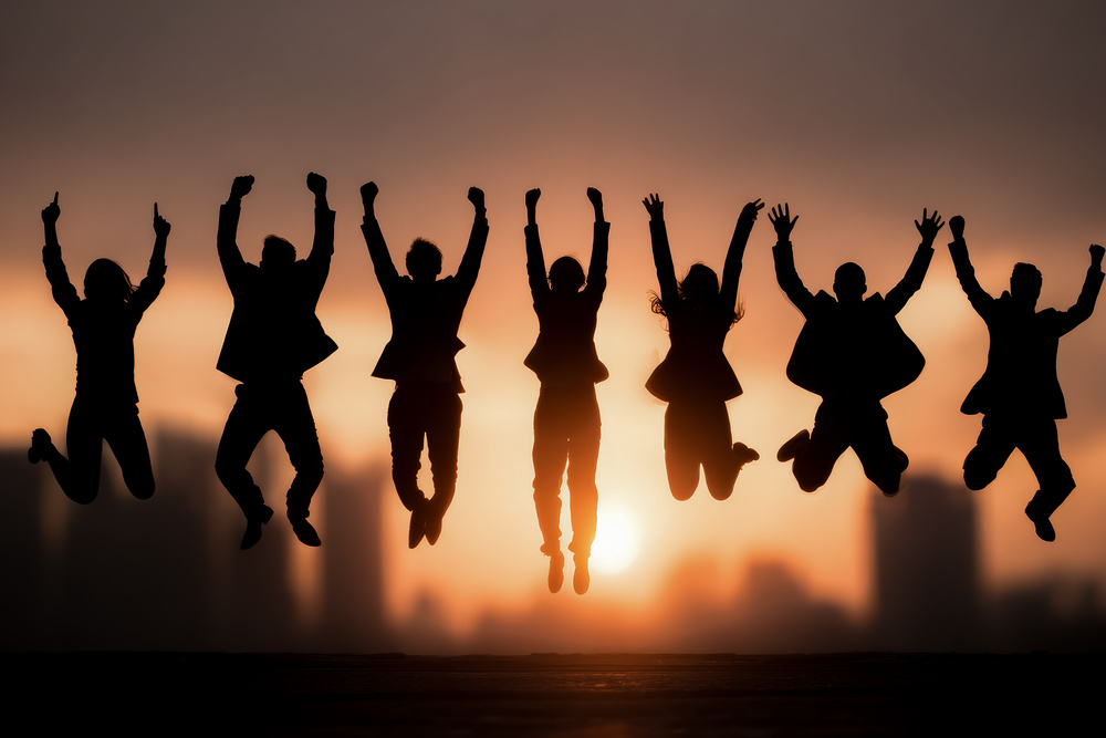 Group of business professionals silhouetted against a sunset, jumping and celebrating career moves and new opportunities in workplace health, wellbeing and culture leadership