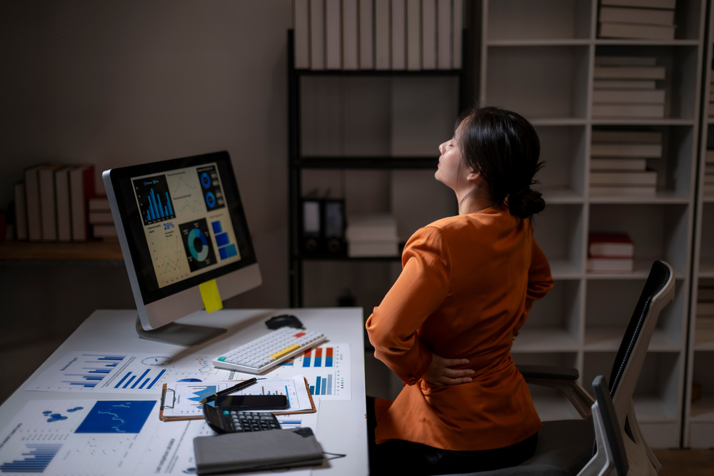 Overworked professional sitting alone late at night in an office, looking exhausted and overwhelmed, symbolising burnout and workaholism