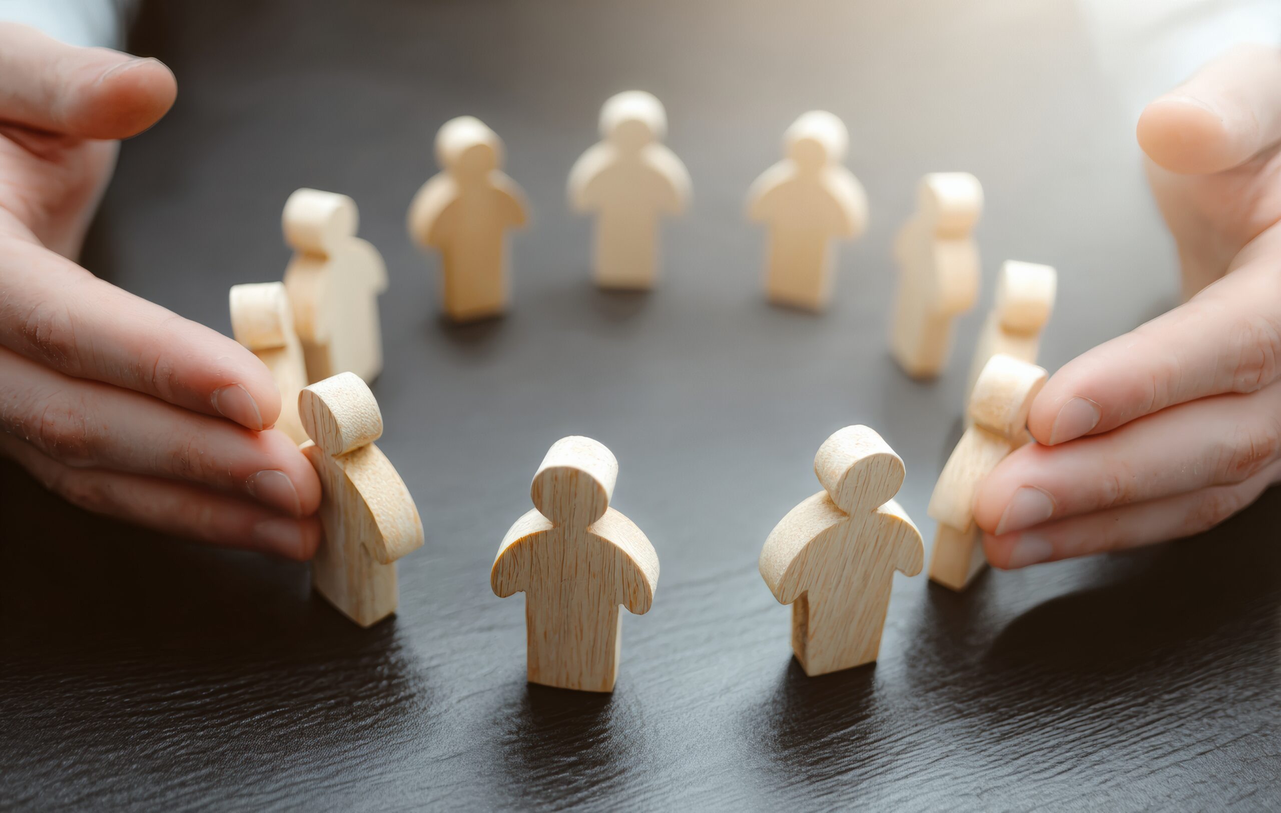 Circle of wooden figures standing together, symbolising an inclusive workplace culture, shared support, employee wellbeing and organisational belonging.