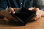 A man sits at a desk looking at an empty wallet, illustrating the hidden impact of financial stress on men's health and wellbeing.