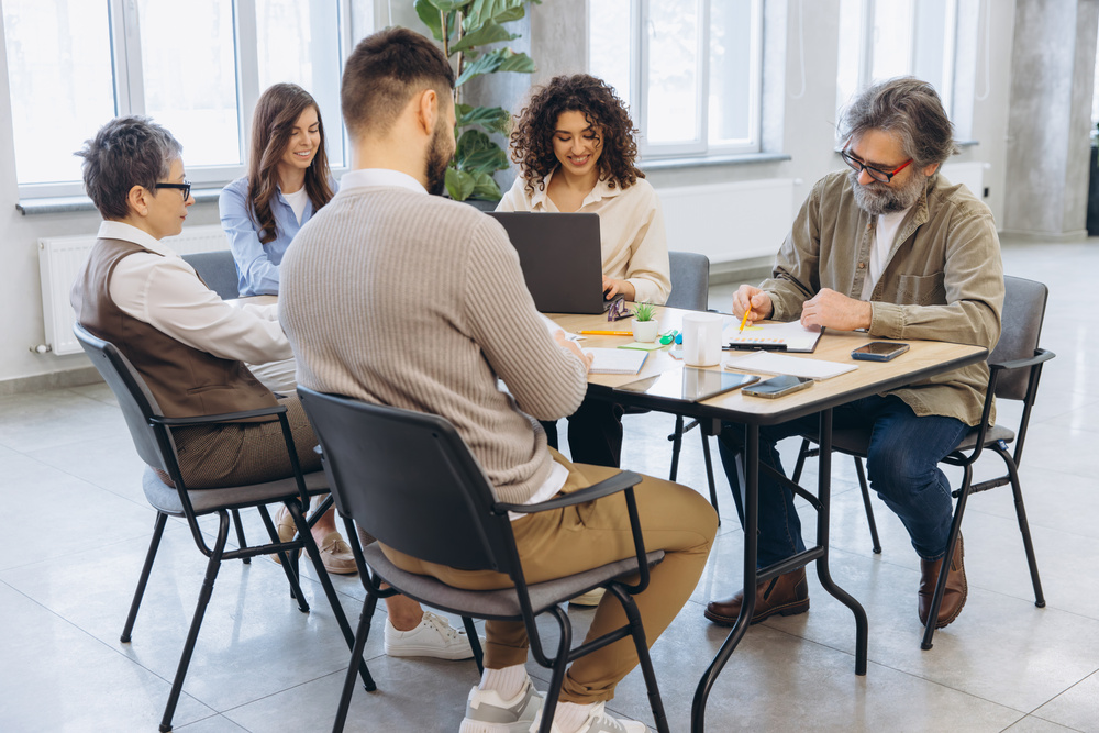 A diverse group of people collaborating around a table, using laptops for a productive meeting.