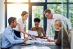 Diverse team of business professionals collaborating and discussing documents in a bright, contemporary office meeting.