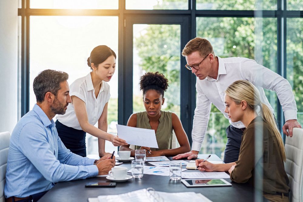 Diverse team of business professionals collaborating and discussing documents in a bright, contemporary office meeting.