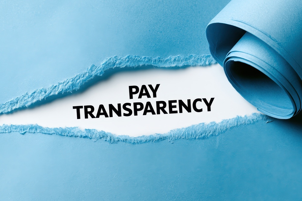 The words "Pay Transparency" revealed beneath torn paper, symbolising greater openness about workplace pay and equal pay reforms.