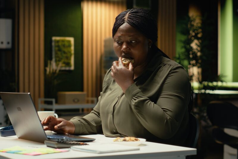 Woman working on a laptop while eating a snack in the evening