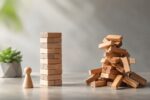 Wooden figure standing beside one intact wooden block tower and one collapsed tower.