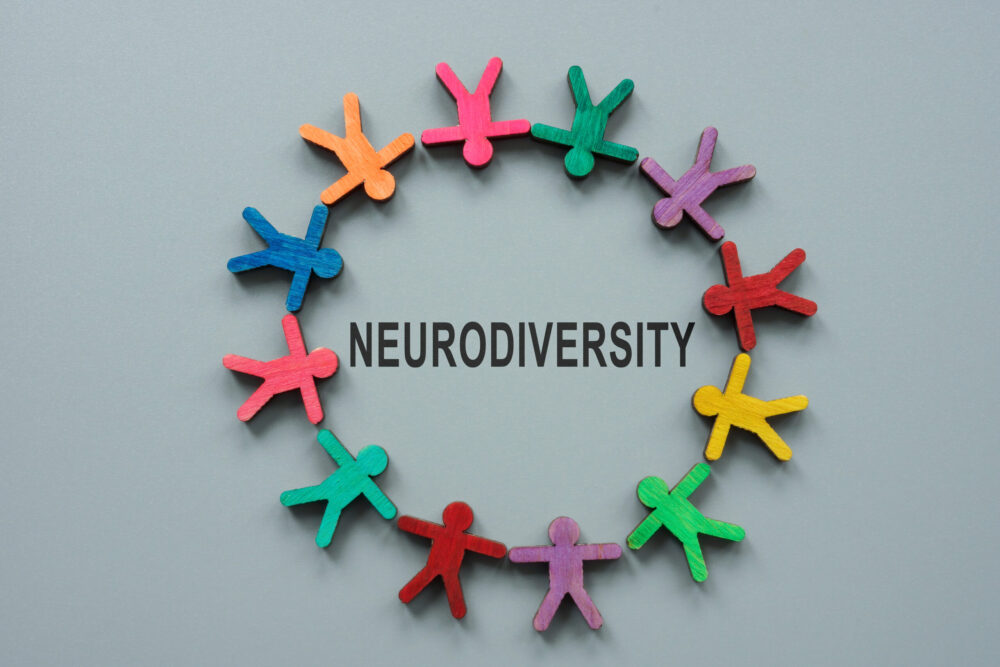 Multicoloured paper cutout people holding hands in a circle around the word “neurodiversity”
