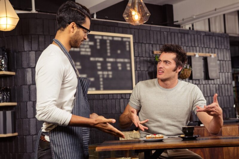 afé worker dealing with a hostile customer complaining at a table.