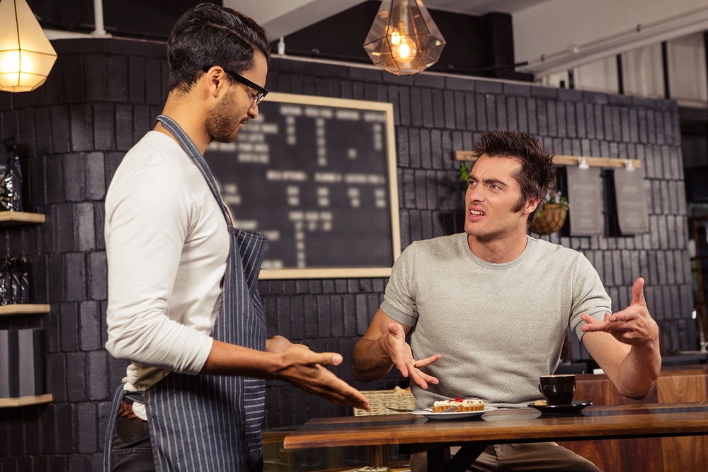 afé worker dealing with a hostile customer complaining at a table.