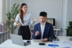 Asian business woman employer expressing anger and frustration towards male employee during a conflict at work, creating stress and a toxic workplace environment