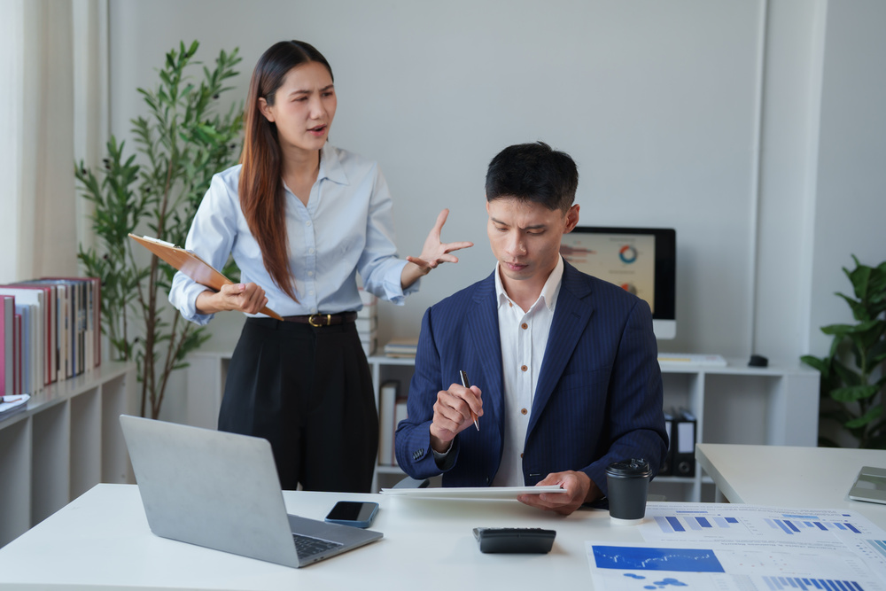 Asian business woman employer expressing anger and frustration towards male employee during a conflict at work, creating stress and a toxic workplace environment
