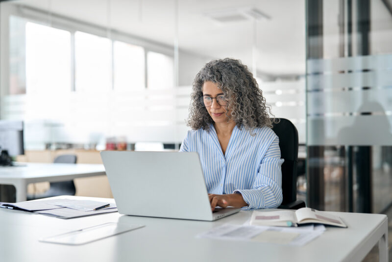 Mature professional woman working on a laptop in a modern office.